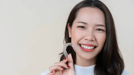 Smiling young woman holding clear aligners for teeth straightening