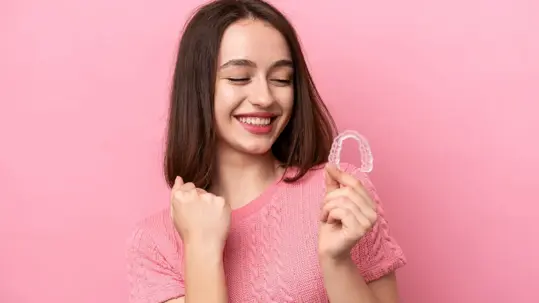 A smiling woman holding up a clear dental aligner or retainer