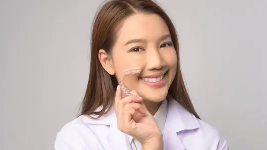 A smiling woman holding a clear dental aligner or retainer