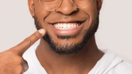 a smiling man pointing at his teeth.