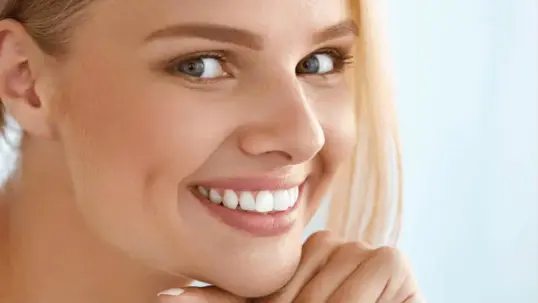 A blonde woman smiles with white teeth