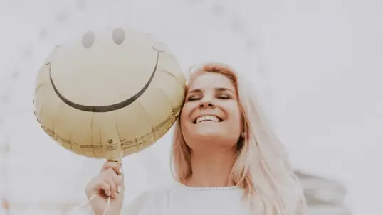 A happy woman is smiling while holding a balloon with a smiley face