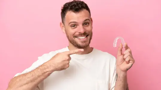 A smiling man points to a clear dental aligner.
